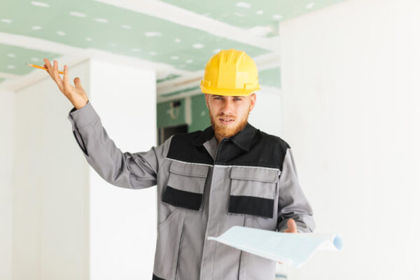 Muncitor în construcții cu cască analizând planuri interioare